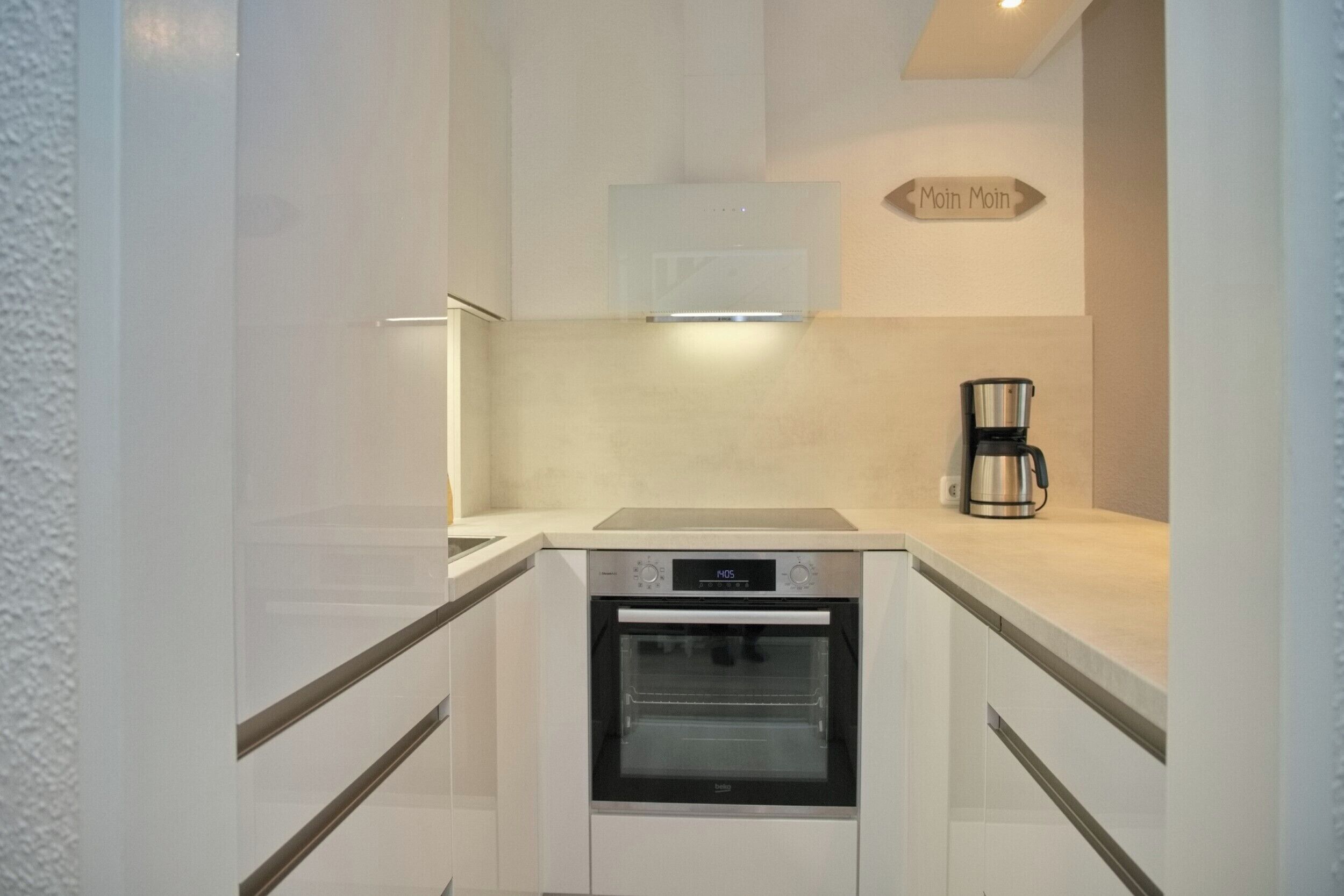 A compact kitchen with a built-in oven, a coffee maker, and a sign indicating the direction to the bathroom.