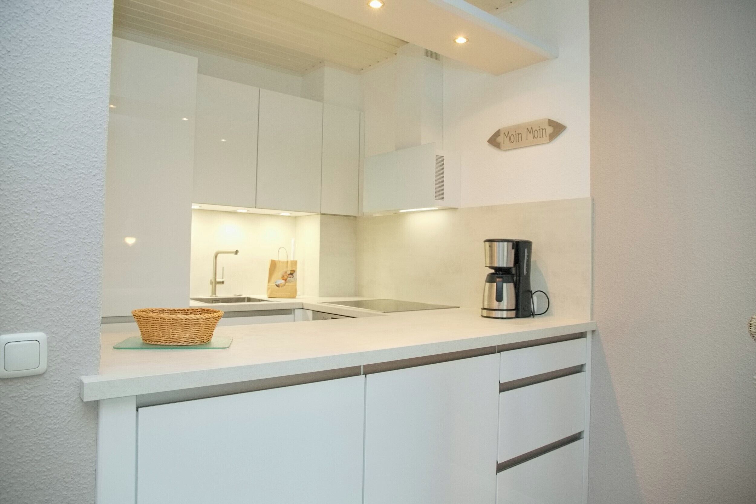 Una cucina moderna con mobili bianchi, una macchina da caffè e un cesto sul piano di lavoro.