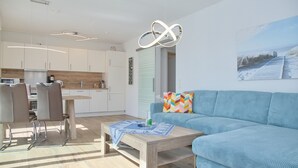 A modern living room with a blue sofa, a wooden coffee table, and a colorful pillow. - Christian-westphal-str. 35, App. Mermaid Inkl. Wlan und Sauna (Grömitz)