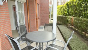 En patio med et rundt bord og fire stole, en murstensvæg og en hæk.