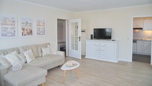 En moderne stue med en sofa, et sofabord og et fjernsyn på et hvidt skab.