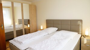 Ein Doppelbett mit weißer Bettwäsche, ein Holzschrank und Nachttischlampen.