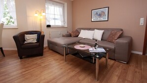Ein Wohnzimmer mit braunem Sofa, einem Glastisch, einem braunen Sessel und einer Stehlampe.