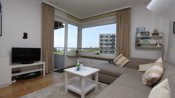 A living room with a flat-screen TV, a white coffee table, a beige sofa, and a view of a building through large windows. - Hanseat II App. 149 Inkl. Wlan (Grömitz)