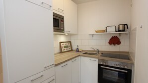 A compact kitchen with white cabinets, a microwave, a sink, and an oven. - Hanseat II App. 149 Inkl. Wlan (Grömitz)