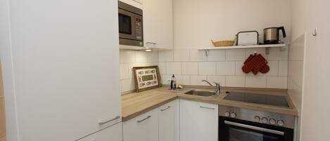 A compact kitchen with white cabinets, a microwave, a sink, and an oven.