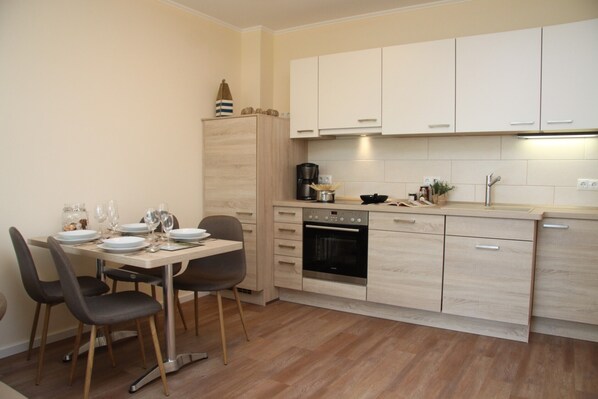 A modern kitchen with light wood cabinets, a built-in oven, and a dining area with a table and chairs.