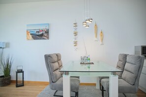 Un comedor moderno con una mesa de vidrio, dos sillas tapizadas, un adorno en la pared y una pequeña planta.