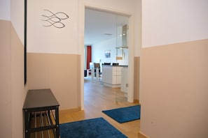 Un pasillo con una mesa negra, alfombras azules y una cocina al fondo.