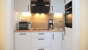 Eine kompakte Küche mit weißen Schränken, einer Mikrowelle, einer Kaffeemaschine und einem eingebauten Backofen.