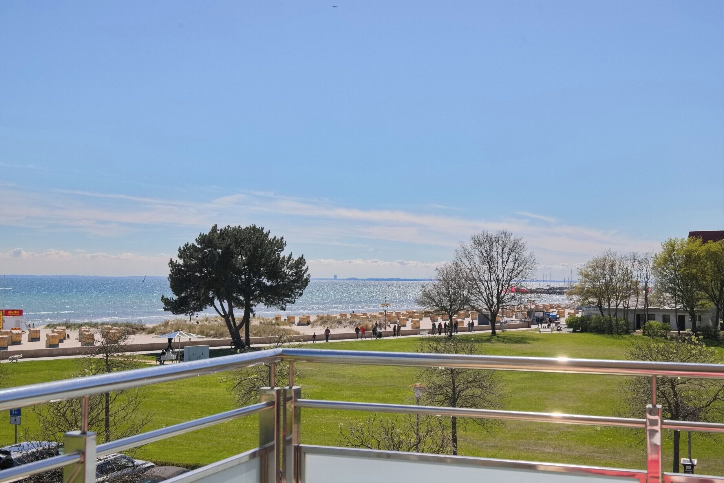A view from a balcony overlooking a beach with a clear sky, a grassy area, and a distant bridge.