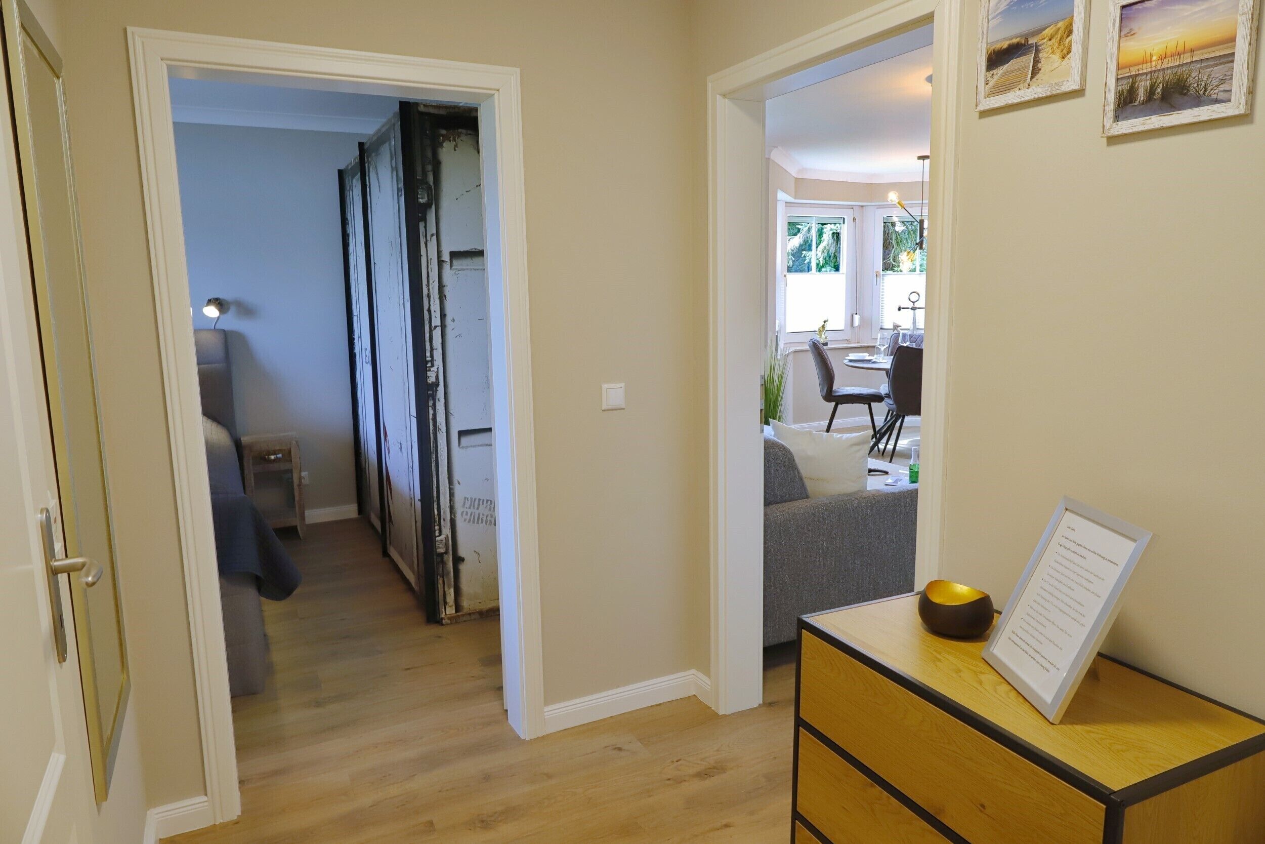 Un pasillo con piso de madera, una pequeña mesa con un tazón y un menú, y una puerta que da a otra habitación.