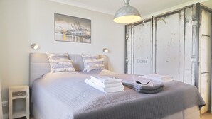 Ein ordentlich bezogenes Bett mit gesteppter Bettdecke, einer Nachttischlampe und einem gefalteten Handtuch.