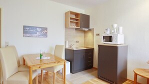 A compact kitchen with a microwave, coffee maker, and a small cabinet. There is a dining table with chairs and a wall-mounted shelf above it. - Dornröschen Wohnung 3 (Grömitz)