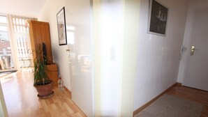 A hallway with wooden flooring, a potted plant, a door with a light switch, and a framed picture on the wall. - Dornröschen Wohnung 3 (Grömitz)
