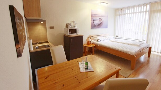 A compact hotel room with a bed, a small kitchenette, a dining table, and a window with curtains. - Dornröschen Wohnung 3 (Grömitz)