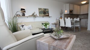 Un salon moderne avec un canapé, une table basse et des plantes décoratives. On aperçoit à l’arrière-plan un coin repas avec des chaises et une table.