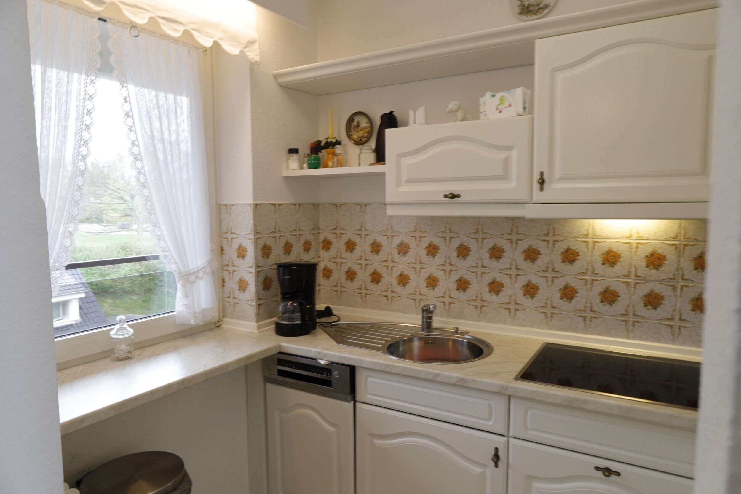 A kitchen with white cabinets, a sink, a coffee maker, and a window with a curtain.