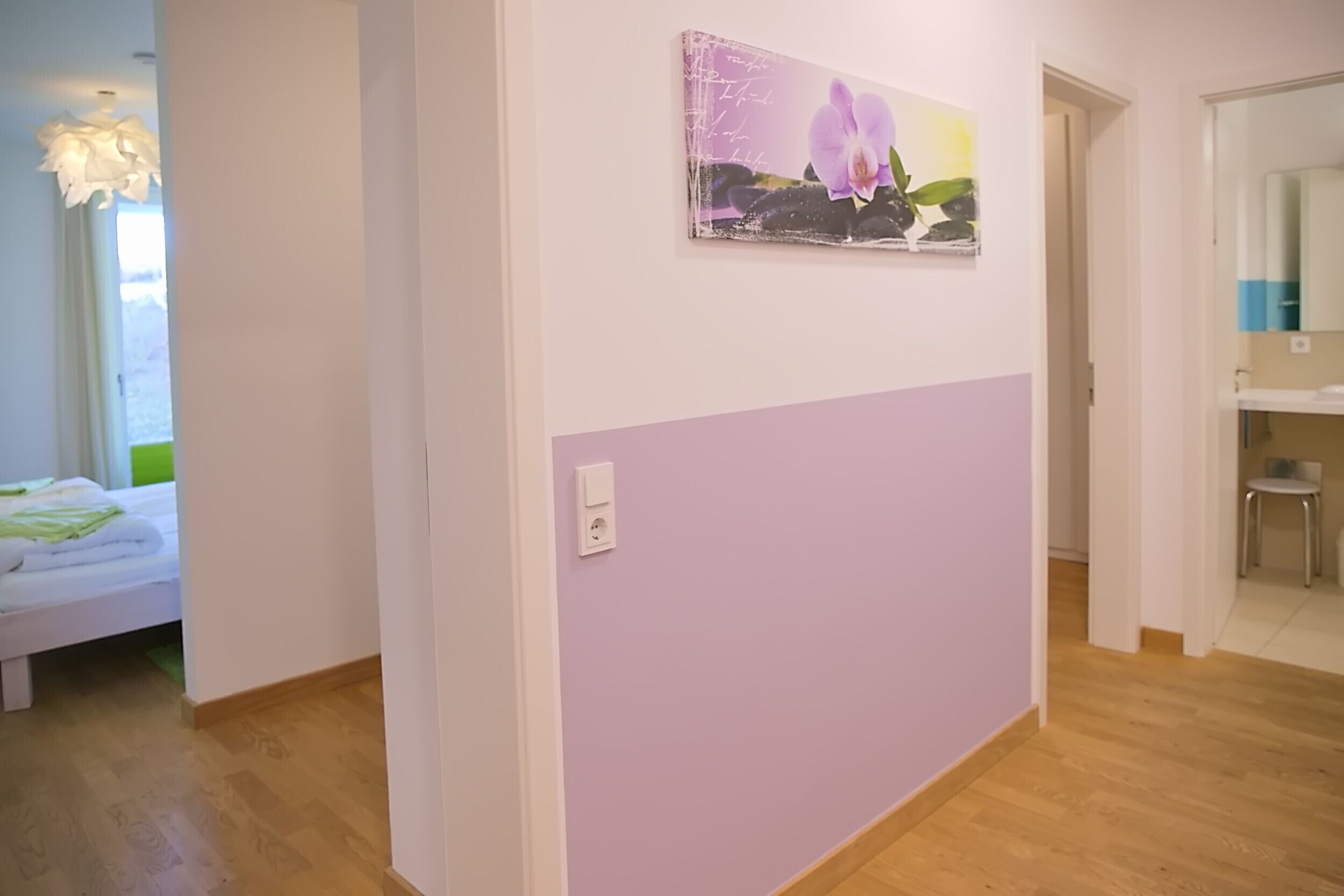 Una habitación con una cama, un cuadro de una orquídea colgado en la pared y suelo de madera.