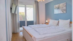 Un dormitorio con una cama, un televisor montado en la pared y una ventana con cortinas.