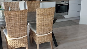Una cocina moderna con armarios blancos, horno empotrado y cafetera. Hay sillas de mimbre alrededor de una mesa de comedor.