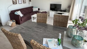 Una sala de estar moderna con una mesa de comedor de madera oscura, sillas de mimbre, un sofá marrón y un televisor de pantalla plana.