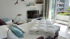 Un dormitorio moderno con una cama grande, un televisor y un balcón con vistas a edificios.