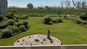 Un jardín ajardinado con un elemento acuático circular, una noria al fondo y un edificio a la izquierda.