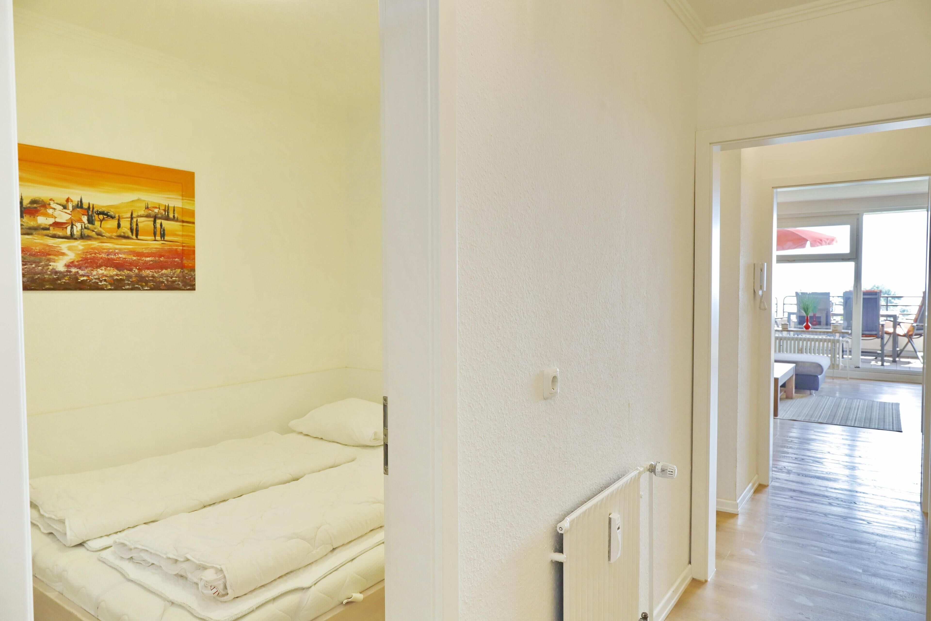A hotel room with a bed, a painting on the wall, and a view of the outdoor area.