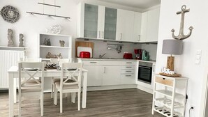 Moderni keittiö, jossa on valkoiset kaapit, valkoisilla tuoleilla varustettu ruokailutila sekä pieni keittiösaareke, jossa on lamppu.
