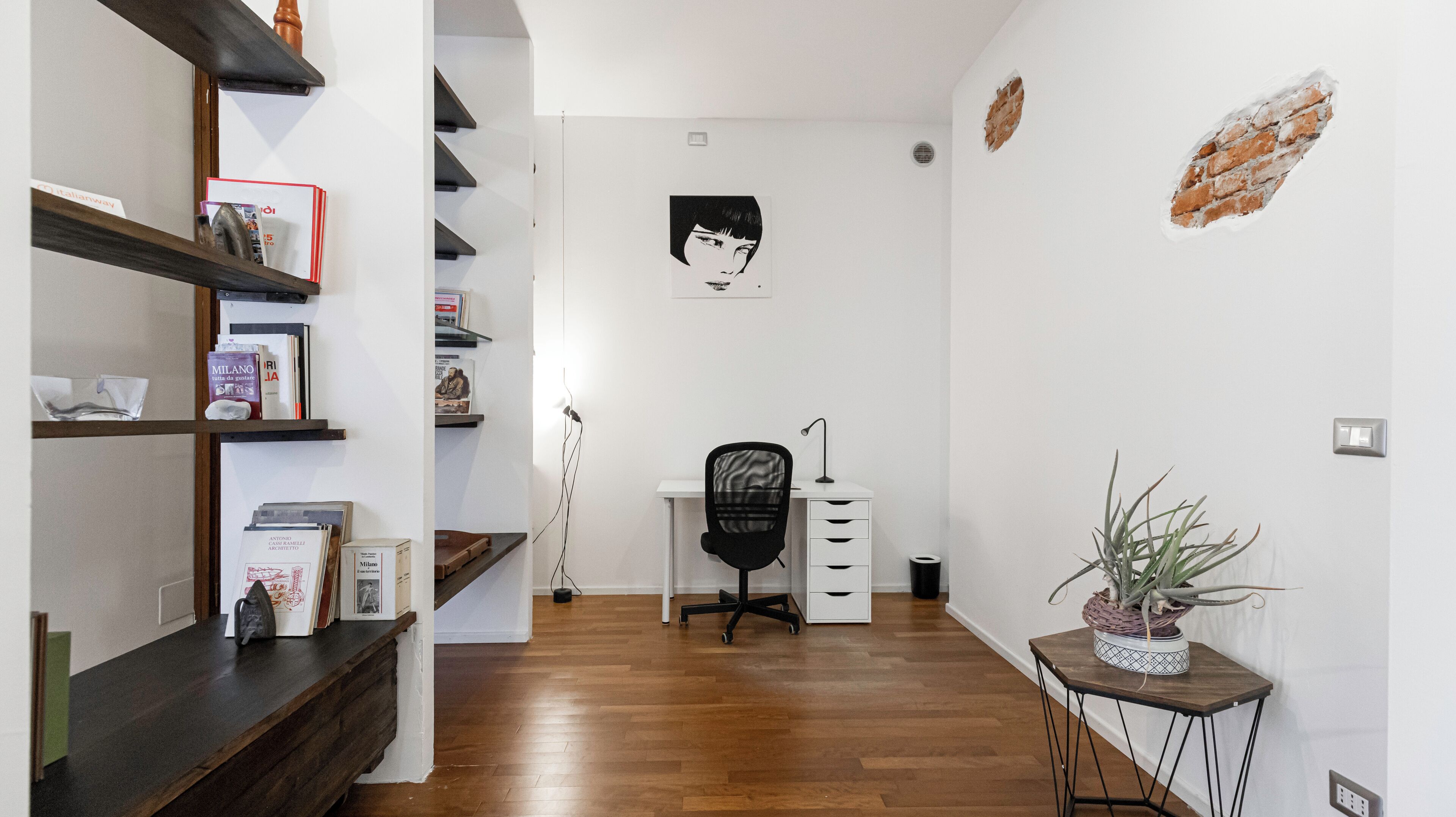 Un espacio de oficina moderno con un escritorio de madera, una silla de oficina negra y una estantería llena de libros y carpetas.