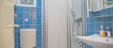 Een badkamer met toilet, douchecabine, wastafel en een handdesinfecterend middel.
