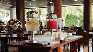 A restaurant with a long wooden table, multiple drink dispensers, and a view of greenery outside. - Ora Beach Resort (El Nido)