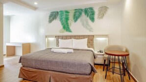 A bedroom with a large bed, a nightstand, a chair, and a wall-mounted lamp. - Ora Beach Resort (El Nido)