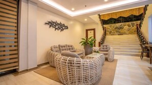 A modern living room with a wicker sofa, a glass coffee table, and a potted plant. A staircase with a stone wall and a wooden railing leads to an upper level. - Ora Beach Resort (El Nido)