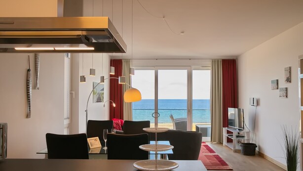 Een moderne woonkamer met een eettafel, een drielaags bijzettafeltje, en uitzicht op de zee door grote ramen.