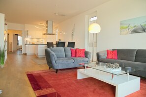 A modern living room with a grey sofa, red cushions, a glass coffee table, and a red rug. - Seeblick Seaside 16 Inkl. Wlan (Grömitz)