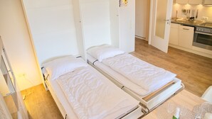 Une chambre avec deux lits simples, une kitchenette et une porte donnant sur une autre pièce.
