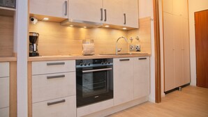 Una cocina moderna con armarios de madera clara, horno empotrado, cafetera y pileta de acero inoxidable.