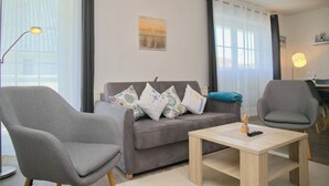 Un salón moderno con un sofá gris, dos sillones, una mesa de centro de madera y una pintura de un paisaje urbano en la pared.