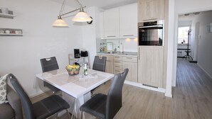 Uma cozinha moderna com armários brancos, forno embutido e uma área de jantar com mesa e cadeiras.