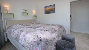 Um quarto com uma cama, abajures, um quadro e uma porta.