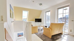 A modern living room with a TV, two yellow armchairs, a small table, and a view of the city through large windows.
