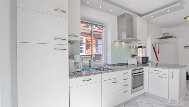 A modern kitchen with white cabinetry, a built-in oven, and a stainless steel range hood.