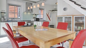 A modern kitchen with a wooden dining table and red chairs, a staircase, and a view of the outside.