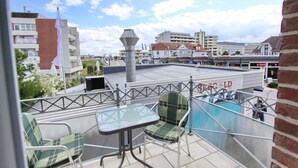 A balcony with a table and chairs, a flag, and buildings in the background.