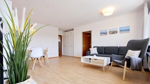A modern living room with a sofa, armchair, coffee table, and a dining area with chairs. - Haus Sonnenblick Whg. 2 Inkl. Wlan (Grömitz)