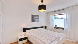 A bedroom with a bed, bedside tables, a lamp, a window with curtains, and a wall-mounted picture. - Haus Sonnenblick Whg. 2 Inkl. Wlan (Grömitz)