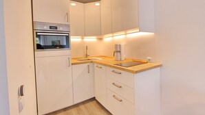 Una cucina moderna con mobili bianchi, forno integrato, macchina del caffè e lavello.