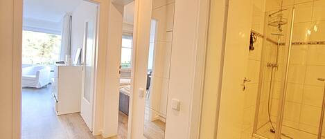 A hotel room with a walk-in closet, a bathroom with a glass shower, and a view of the garden.